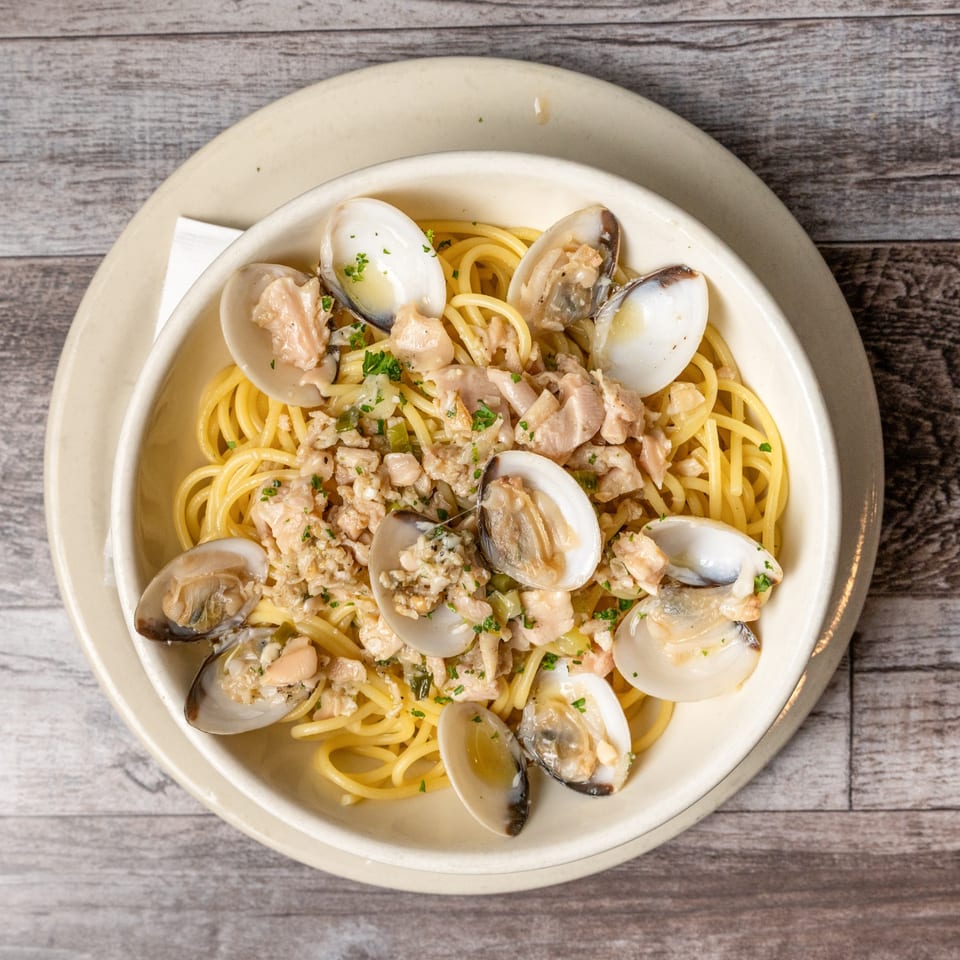 Spaghetti with clams and parsley in a white bowl on a wooden table.