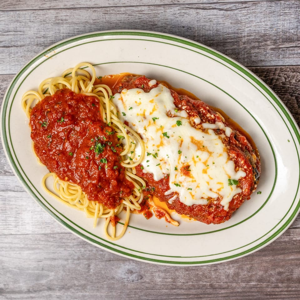 Chicken parmesan with spaghetti and marinara sauce on a white plate with green stripes.