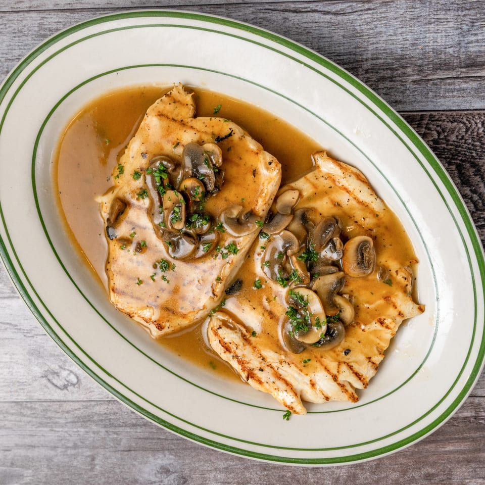 Grilled chicken breasts with mushroom gravy and parsley on a white oval plate with green stripes.