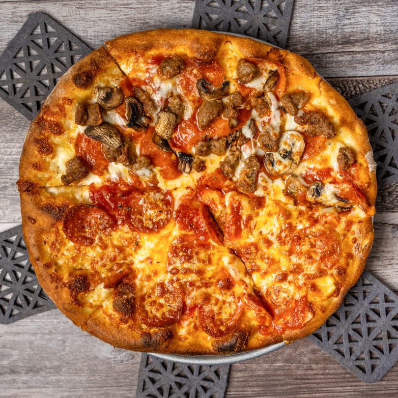 Overhead view of a half pepperoni, half sausage and mushroom pizza on a wooden table.