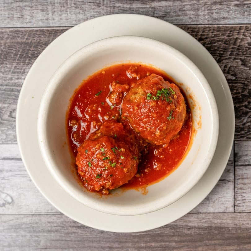 Two large meatballs covered in red marinara sauce and parsley in a white bowl.
